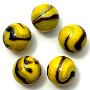 Può includere: Cinque biglie di vetro con un motivo a spirale giallo e marrone scuro. Le biglie sono rotonde e hanno una finitura lucida. Le biglie sono disposte in un motivo circolare su uno sfondo bianco.