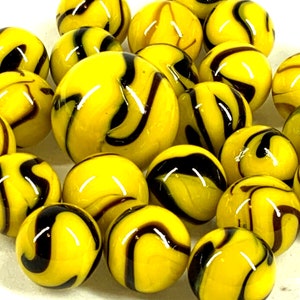 May include: A collection of yellow glass marbles with dark brown and black swirling patterns. The marbles are round and glossy, with a variety of patterns. The marbles are a classic toy, perfect for collectors or for playing games.