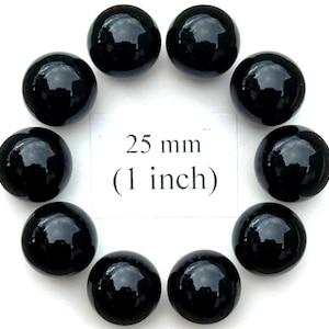 May include: Ten glossy black spheres, each approximately 1 inch in diameter, arranged in a circular pattern. A white card in the center displays the text "25 mm (1 inch)". The spheres have a reflective surface.