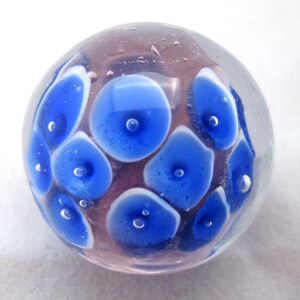 May include: A clear glass sphere with blue and white circles inside. The circles have a white outline and a small blue dot in the center.