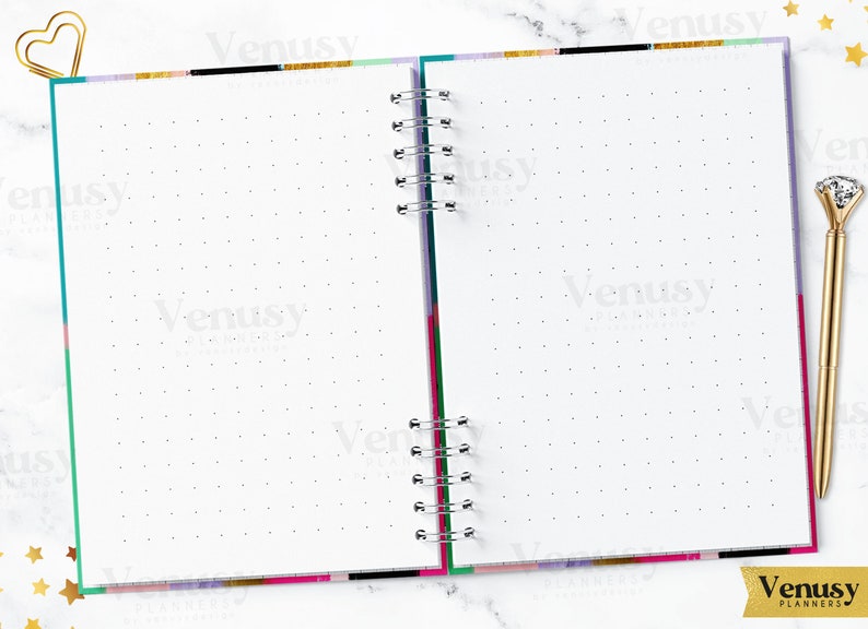 Puede incluir: Cuaderno abierto con espiral y p&aacute;ginas de puntos. El cuaderno tiene un borde colorido con rayas doradas, negras, rosas y turquesas. Un clip de papel dorado en forma de coraz&oacute;n y un bol&iacute;grafo con punta de diamante est&aacute;n en la p&aacute;gina.