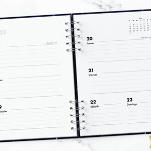 May include: A two-page spread from a July 2023 planner with a black and white starry design. The left page shows the dates 17, 18, and 19 with the days of the week listed as Lunes, Martes, and Mi&eacute;rcoles. The right page shows the dates 20, 21, 22, and 23 with the days of the week listed as Jueves, Viernes, S&aacute;bado, and Domingo. The right page also includes a small calendar for the month of August.
