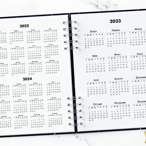 May include: A black and white calendar planner with a galaxy design. The planner includes the months of January through December for the years 2022, 2023, and 2024. The planner is open to the months of July, August, and September of 2023.