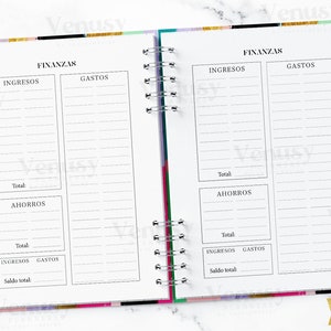 Puede incluir: Planificador abierto con encabezados "FINANZAS" y secciones para "INGRESOS", "GASTOS" y "AHORROS". Las p&aacute;ginas son blancas con l&iacute;neas y texto en negro. Se ve un bol&iacute;grafo dorado con una parte superior en forma de diamante y un clip de papel dorado en forma de coraz&oacute;n.