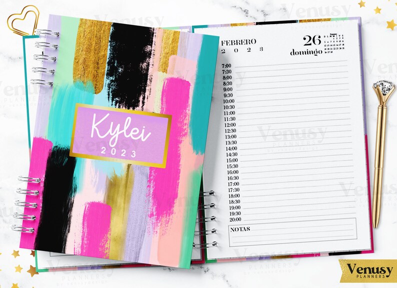 Puede incluir: Una agenda con espiral con un dise&ntilde;o abstracto colorido. La portada presenta pinceladas audaces en oro, negro, rosa y turquesa, con el nombre "Kylei" y el a&ntilde;o "2023" en un rect&aacute;ngulo dorado. La p&aacute;gina abierta muestra un horario diario.