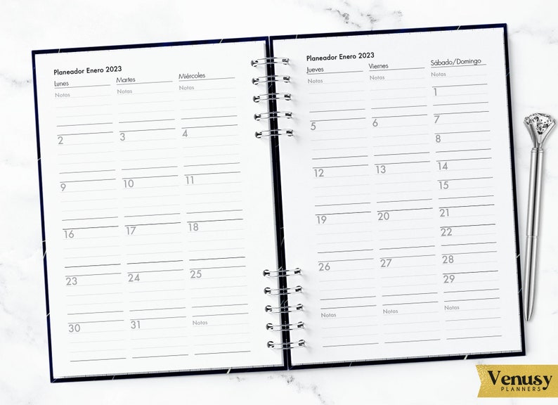 May include: A black and white planner with a silver coil binding. The planner is open to January 2023 and has a Spanish title "Planeador Enero 2023". The planner has columns for each day of the week, with spaces for notes.