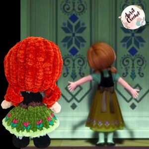 Op de afbeelding: Een handgemaakte gehaakte pop van een personage met rood haar, gekleed in een groene en zwarte jurk. De pop staat voor een cartoonafbeelding van hetzelfde personage. De pop heeft een zachte textuur en is waarschijnlijk gemaakt van garen.
