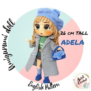 Può includere: Schema per bambola all'uncinetto per una bambola alta 26 cm di nome Adela. La bambola indossa un berretto blu, un cappotto grigio, una camicia a righe verdi e bianche, una gonna blu e stivali blu. Tiene una borsa blu. Lo schema è scritto in inglese.