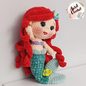 Puede incluir: Mu&ntilde;eca de sirena de ganchillo hecha a mano con cabello rojo, top morado y cola turquesa. La mu&ntilde;eca tiene una flor amarilla en la cola y lleva una flor azul en el pelo. La mu&ntilde;eca est&aacute; hecha de hilo suave y afelpado.