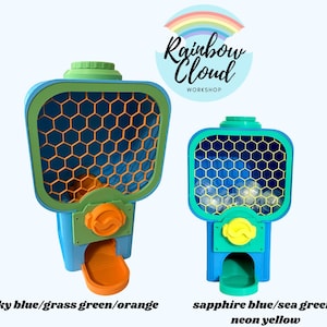 Op de afbeelding: Twee kleurrijke kauwgomballenautomaten. E&eacute;n is hemelsblauw, grasgroen en oranje. De andere is saffierblauw, zeegroen en neongeel. Beide hebben een honingraatpatroon aan de voorkant. De tekst "Rainbow Cloud Workshop" staat op de achtergrond.