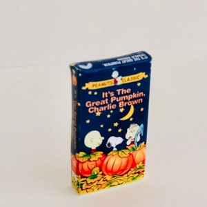 Op de afbeelding: Een blauwe en gele doos met een Peanuts-cartoonillustratie. De doos toont Charlie Brown, Snoopy en Linus. De tekst op de doos luidt "It's The Great Pumpkin, Charlie Brown".