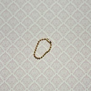 May include: A small gold-toned ball chain connector, also known as a bead chain connector, featuring a series of tiny spherical metal beads linked together in a circular loop with a cylindrical clasp mechanism to secure the ends.