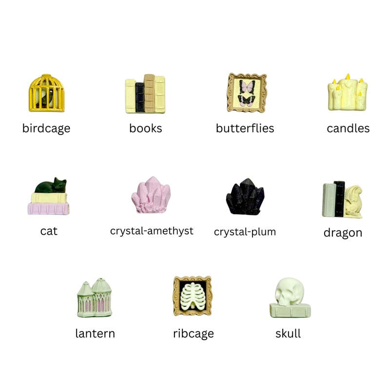 May include: A collection of eleven miniature decorative figurines including a yellow birdcage, books, framed butterflies, candles, a cat on books, amethyst and plum crystals, a dragon, a lantern, a framed ribcage, and a skull on a book.