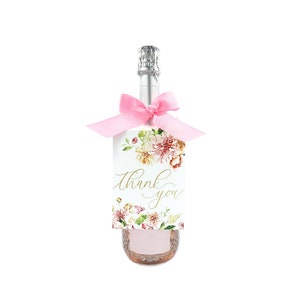 May include: A small bottle of champagne with a pink ribbon and a white tag that says "Thank you" with floral designs.
