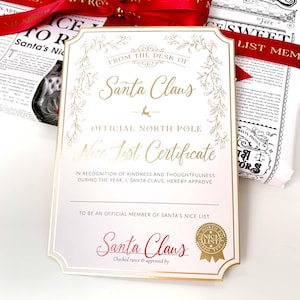 May include: A Christmas-themed certificate from Santa Claus, with gold lettering and a decorative border. The certificate reads "Nice List Certificate" and includes the text "Checked twice & approved by Santa Claus". A red ribbon is visible.