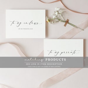 May include: Two white cards with black calligraphy. The top card says "To my in-laws" and the bottom card says "To my parents". Both cards have the text "On my wedding day" underneath the main text. The cards are on a light pink background with a white flower and a pink ribbon.