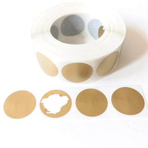 May include: A roll of gold round stickers on a white background. The stickers are arranged in a circle around the roll. There are also four individual stickers on the white background.