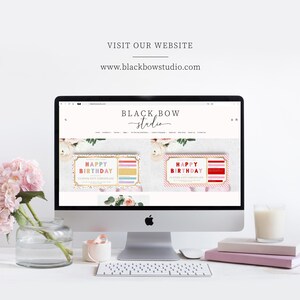 May include: A desktop computer displays the Black Bow Studio website, showcasing birthday gift certificates. The screen is surrounded by a vase of pink flowers, a candle, books, and a keyboard. The website address is www.blackbowstudio.com.