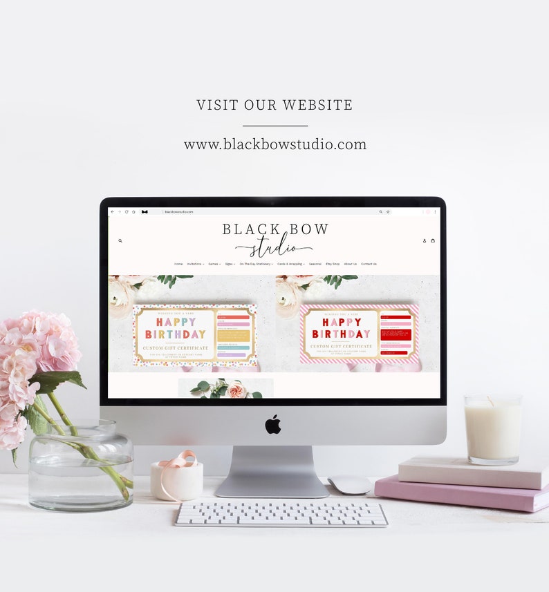 May include: A desktop computer displays the Black Bow Studio website, showcasing birthday gift certificates. The screen is surrounded by a vase of pink flowers, a candle, books, and a keyboard. The website address is www.blackbowstudio.com.