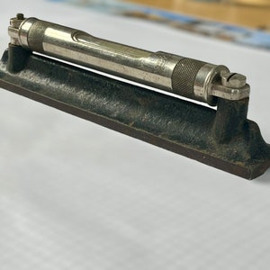 May include: A vintage metal level with a black base and a silver metal level attached to the top. The level has a small bubble in the centre of the level.
