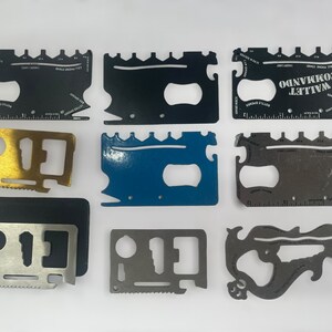 May include: A collection of ten multi-tool credit card sized pocket knives. The knives are made of metal and have various tools, including a bottle opener, a ruler, a screwdriver, and a saw. The knives are in different colours, including black, silver, gold, and blue.