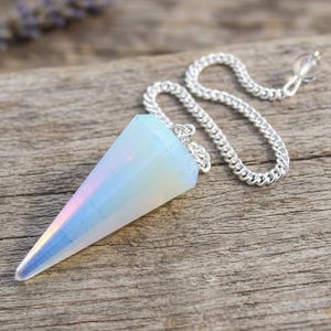 May include: A faceted, cone-shaped opalite pendant with a smooth, translucent, milky white appearance and subtle iridescent blue and pink highlights. The pendant is attached to a silver-toned metal chain with small, interlocking links.