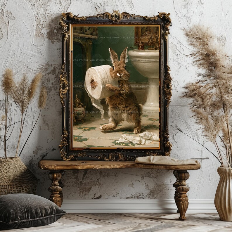 May include: A framed wall art print featuring a brown rabbit standing in a bathroom, holding a roll of white toilet paper. The rabbit is positioned on a tiled floor near a white pedestal sink. The frame is ornate, dark, and metallic in color.
