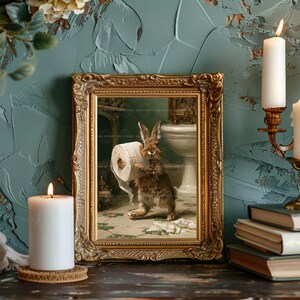 May include: A framed wall art print featuring a brown rabbit standing in a bathroom, holding a roll of white toilet paper. The artwork is encased in an ornate, antique-style gold frame with intricate detailing along the edges and corners.