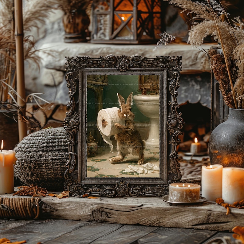 May include: A rectangular, ornate, dark-toned picture frame containing an illustration of a brown rabbit standing on a tiled floor while holding a roll of white toilet paper in a bathroom setting with a white pedestal sink in the background.