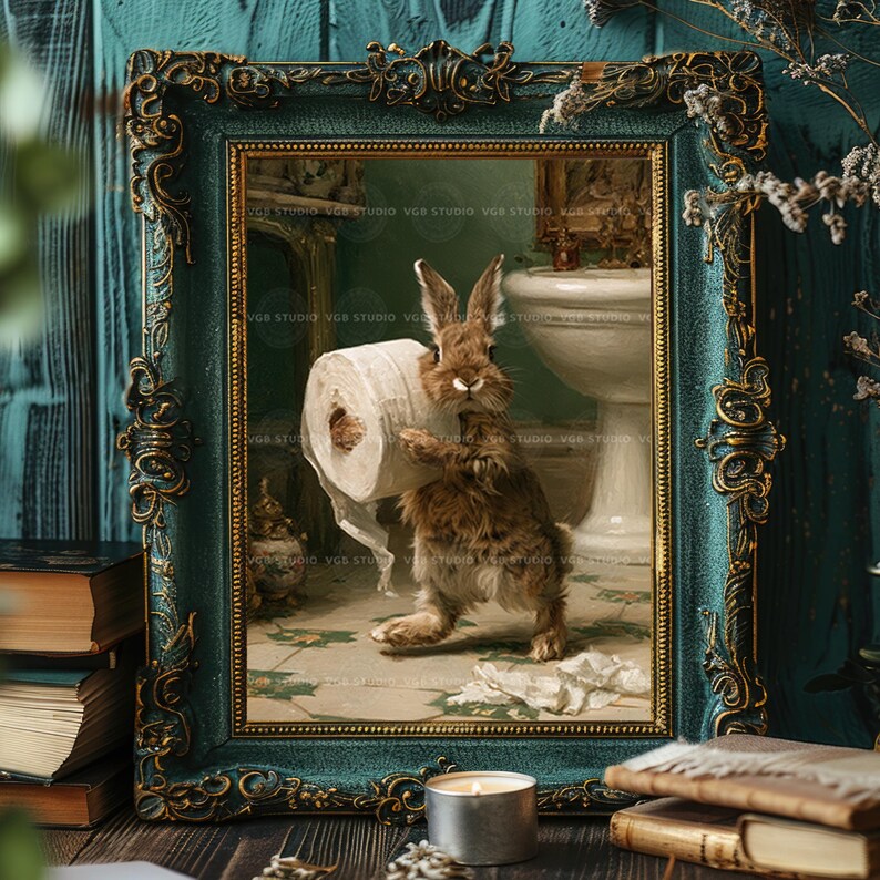 May include: A framed wall art print featuring a brown rabbit standing in a bathroom and holding a roll of white toilet paper. The frame is ornate, dark teal with gold accents. The artwork depicts a sink and tiled floor in the background.
