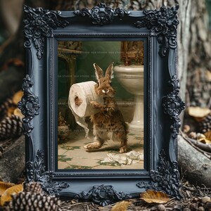May include: A brown rabbit stands in a bathroom holding a roll of white toilet paper. The scene is enclosed in a dark, ornate, rectangular frame with intricate floral carvings. The background shows a white pedestal sink and a green tiled floor.