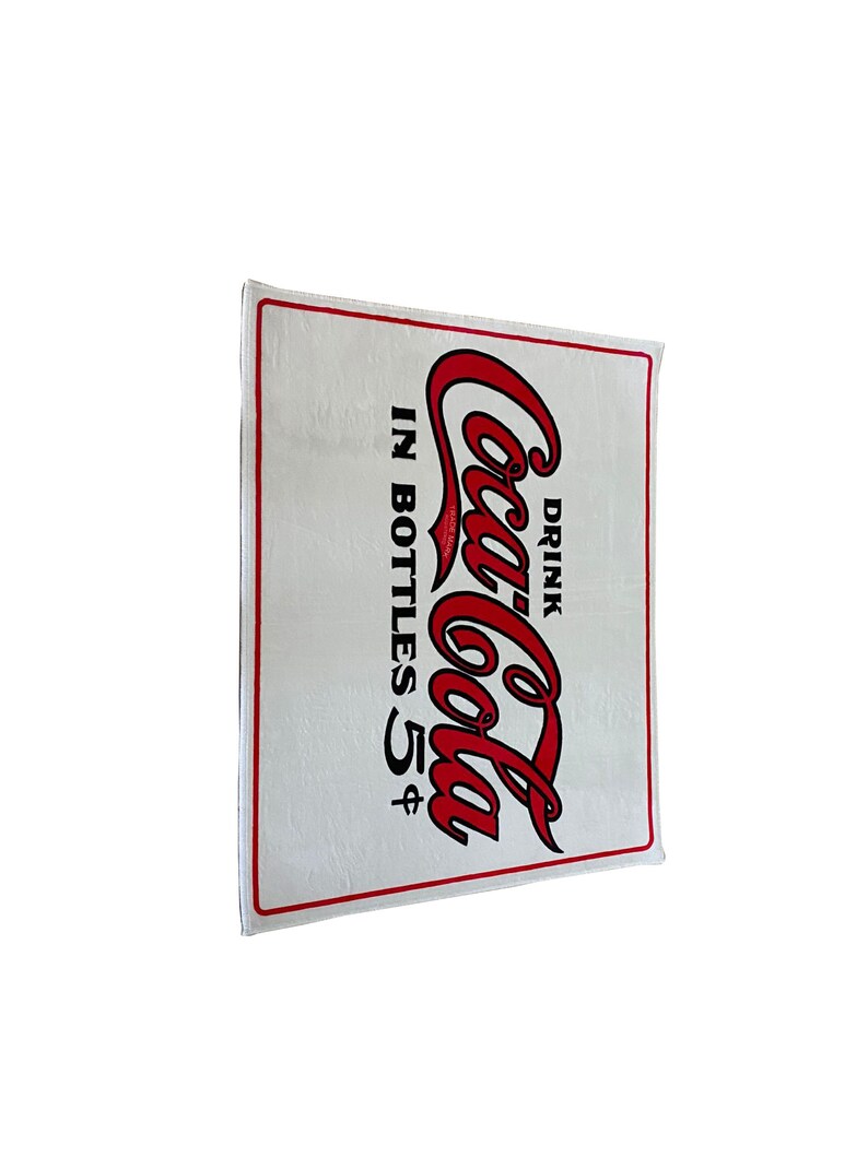K&ouml;nnte beinhalten: Ein wei&szlig;es rechteckiges Schild mit einem roten Coca-Cola-Logo und dem Text "Drink Coca-Cola in bottles 5&cent;".