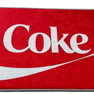 May include: Red doormat with a white Coca-Cola logo and a white wave design.