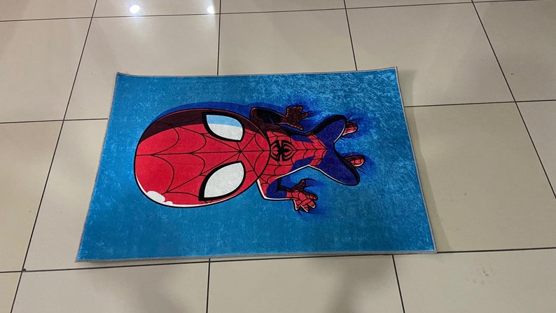 May include: A blue rug with a cartoon image of Spiderman in a red and blue suit. The rug is made of a soft, plush material.