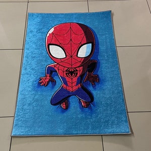 May include: A blue rug with a cartoon image of Spiderman in a red and blue suit. The Spiderman character is in a crouching position with his arms outstretched.