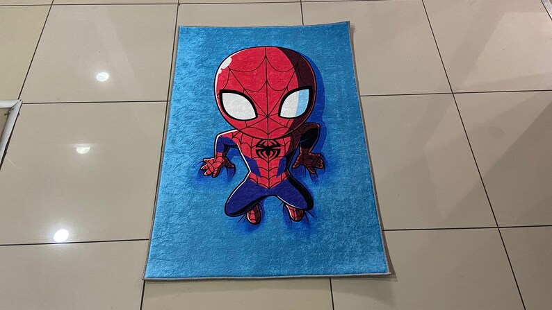 May include: A blue rug with a cartoon image of Spiderman in a red and blue suit. The Spiderman character is in a crouching position with his arms outstretched.