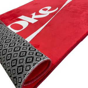 May include: Red doormat with the word "Coke" in white lettering and a white wave design. The doormat has a black and white geometric pattern on the back.