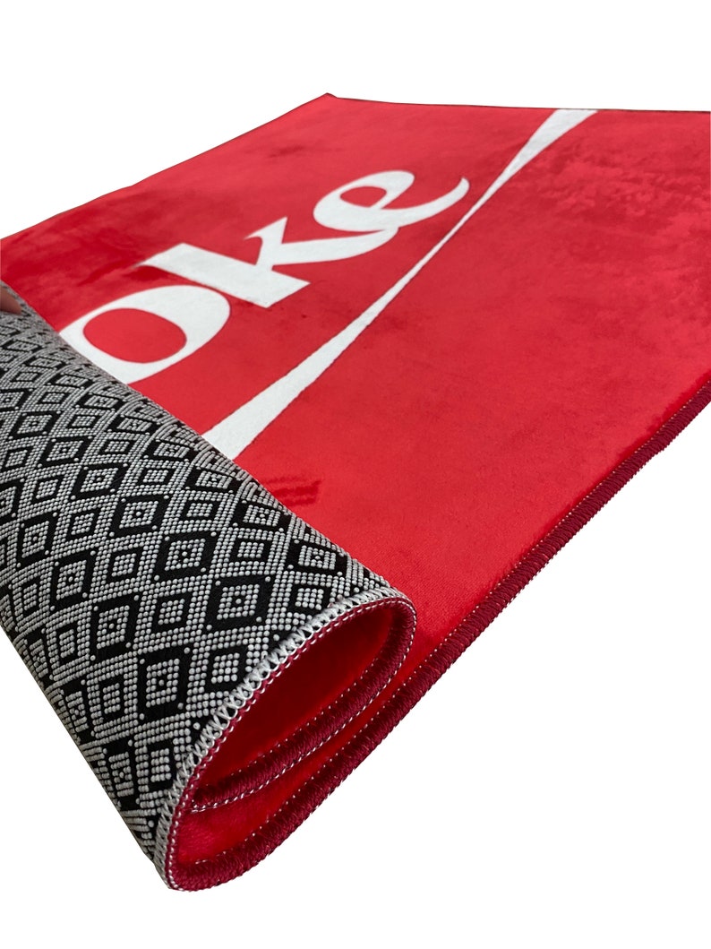May include: Red doormat with the word "Coke" in white lettering and a white wave design. The doormat has a black and white geometric pattern on the back.