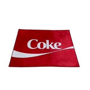 May include: Red rectangular rug with a white Coca-Cola logo and a white wave design.