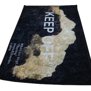 Pu&ograve; includere: Tappeto nero e bianco con un testo bianco "KEEP OFF" e un design astratto marrone e bianco. Il tappeto ha il testo "IKEA&reg; c/o Virgil Abloh&trade; Flooring" e "Almhult, Svezia &copy;2019" in bianco.