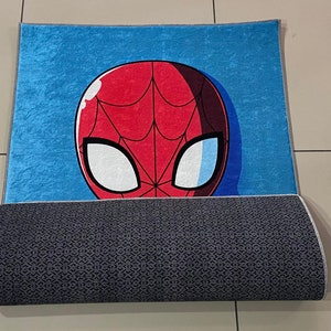 May include: A blue and red rug with a cartoon image of Spider-Man's face. The rug has a gray backing.