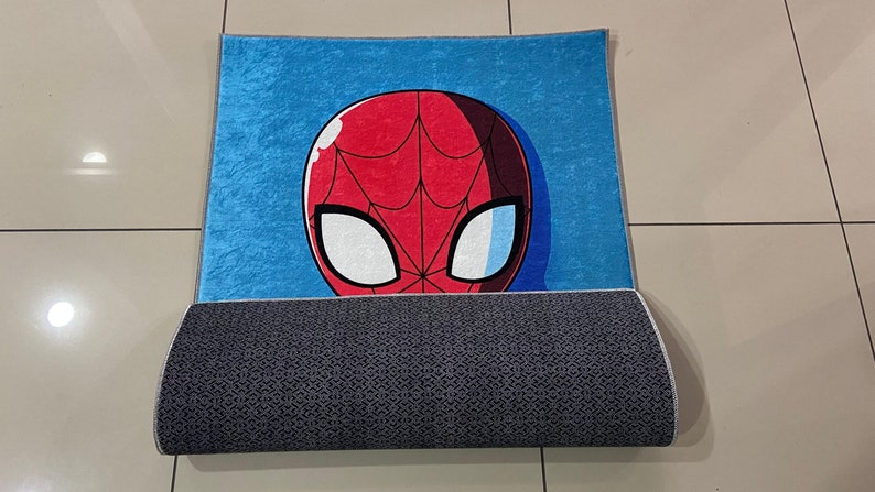 May include: A blue and red rug with a cartoon image of Spider-Man's face. The rug has a gray backing.