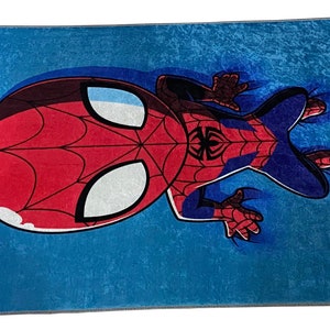 May include: A blue rug with a cartoon image of Spiderman in a red and blue suit. Spiderman is upside down with his head and one leg in the air.