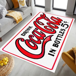 K&ouml;nnte beinhalten: Wei&szlig;er Coca-Cola-Teppich mit roter Aufschrift "Drink Coca-Cola in Bottles 5&cent;" und einem roten Logo "Trade Mark Registered".