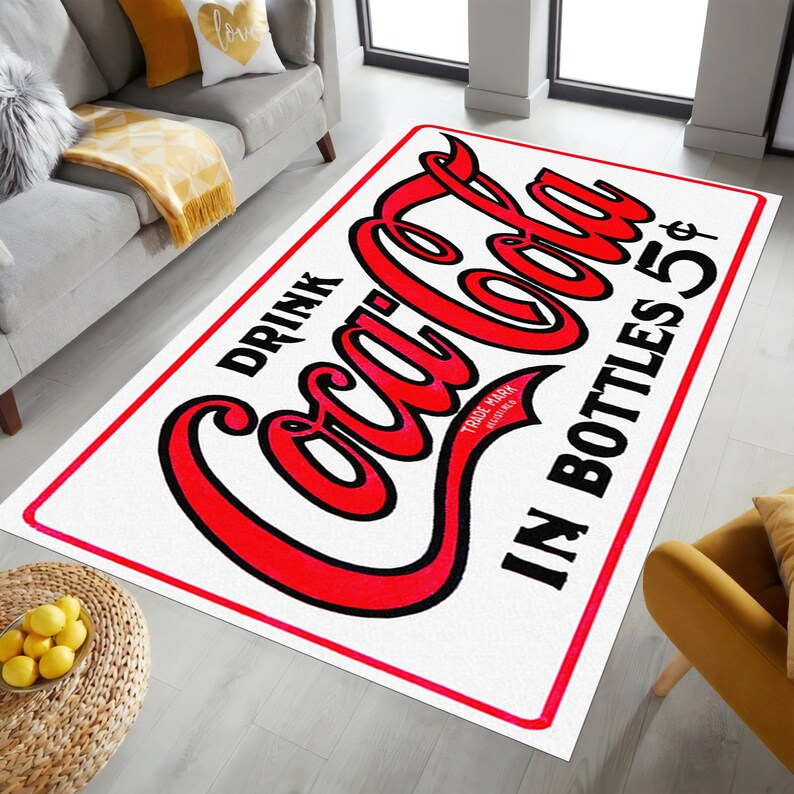 K&ouml;nnte beinhalten: Wei&szlig;er Coca-Cola-Teppich mit roter Aufschrift "Drink Coca-Cola in Bottles 5&cent;" und einem roten Logo "Trade Mark Registered".