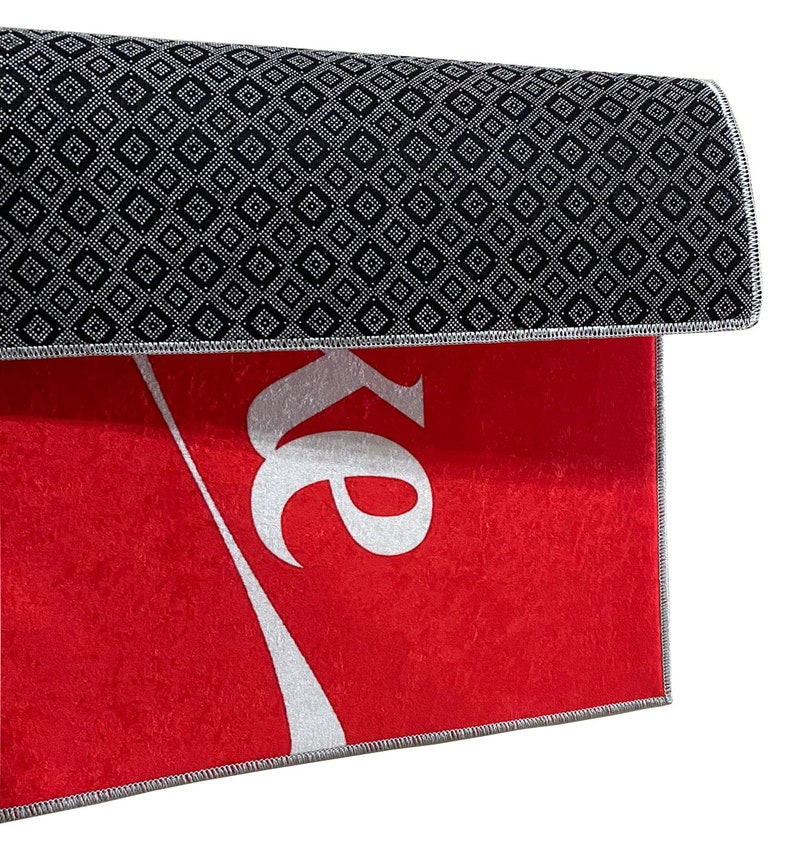May include: Red doormat with a white Coca-Cola logo. The back of the doormat has a black diamond pattern.