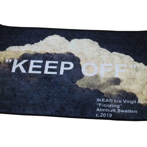 Pu&ograve; includere: Un tappetino da porta nero con un design a nuvola bianca e il testo "KEEP OFF" in bianco. Il tappetino include anche il testo "IKEA&reg; c/o Virgil Abloh&trade; "Flooring" Almhult, Svezia c.2019".