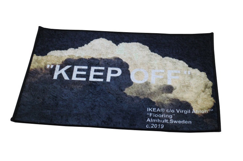 Pu&ograve; includere: Un tappetino da porta nero con un design a nuvola bianca e il testo "KEEP OFF" in bianco. Il tappetino include anche il testo "IKEA&reg; c/o Virgil Abloh&trade; "Flooring" Almhult, Svezia c.2019".