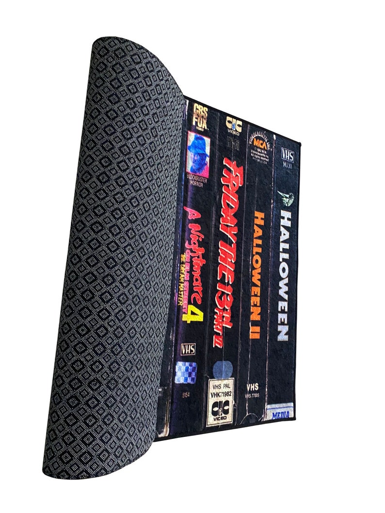 May include: A stack of VHS tapes with the titles "Halloween", "Halloween II", "Friday the 13th", and "A Nightmare on Elm Street 4" on a black and white patterned surface.