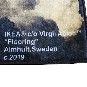 Pu&ograve; includere: Primo piano di un tappeto nero e bianco con un motivo sbiadito. Il tappeto ha un bordo nero e testo bianco che recita "IKEA&reg; c/o Virgil Abloh&trade; "Flooring" Almhuult, Svezia c.2019"
